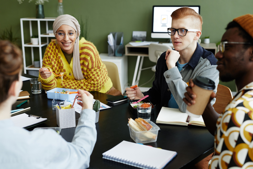 Portrait of creative young man working with diverse design team at business meeting and enjoying snacks